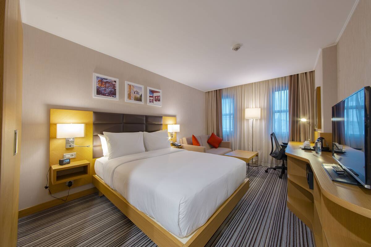 A hotel room with a large bed, bedside tables with lamps, a desk with a TV, and a chair.
