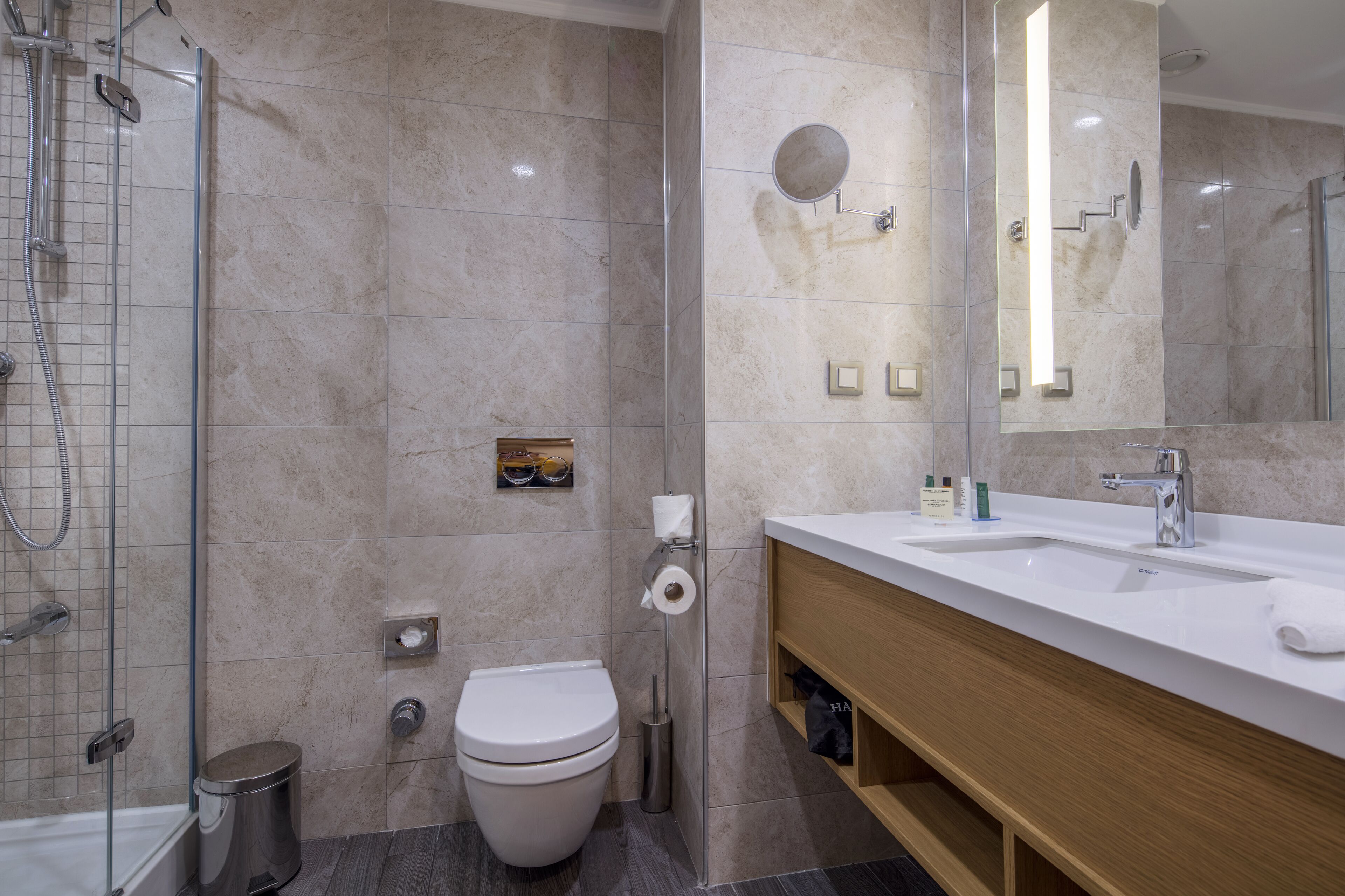 Un baño moderno con ducha acristalada, inodoro y tocador con lavabo y espejo.