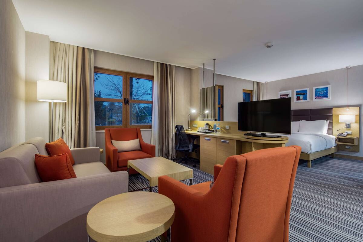 A hotel room with a sofa, armchair, desk, and bed.