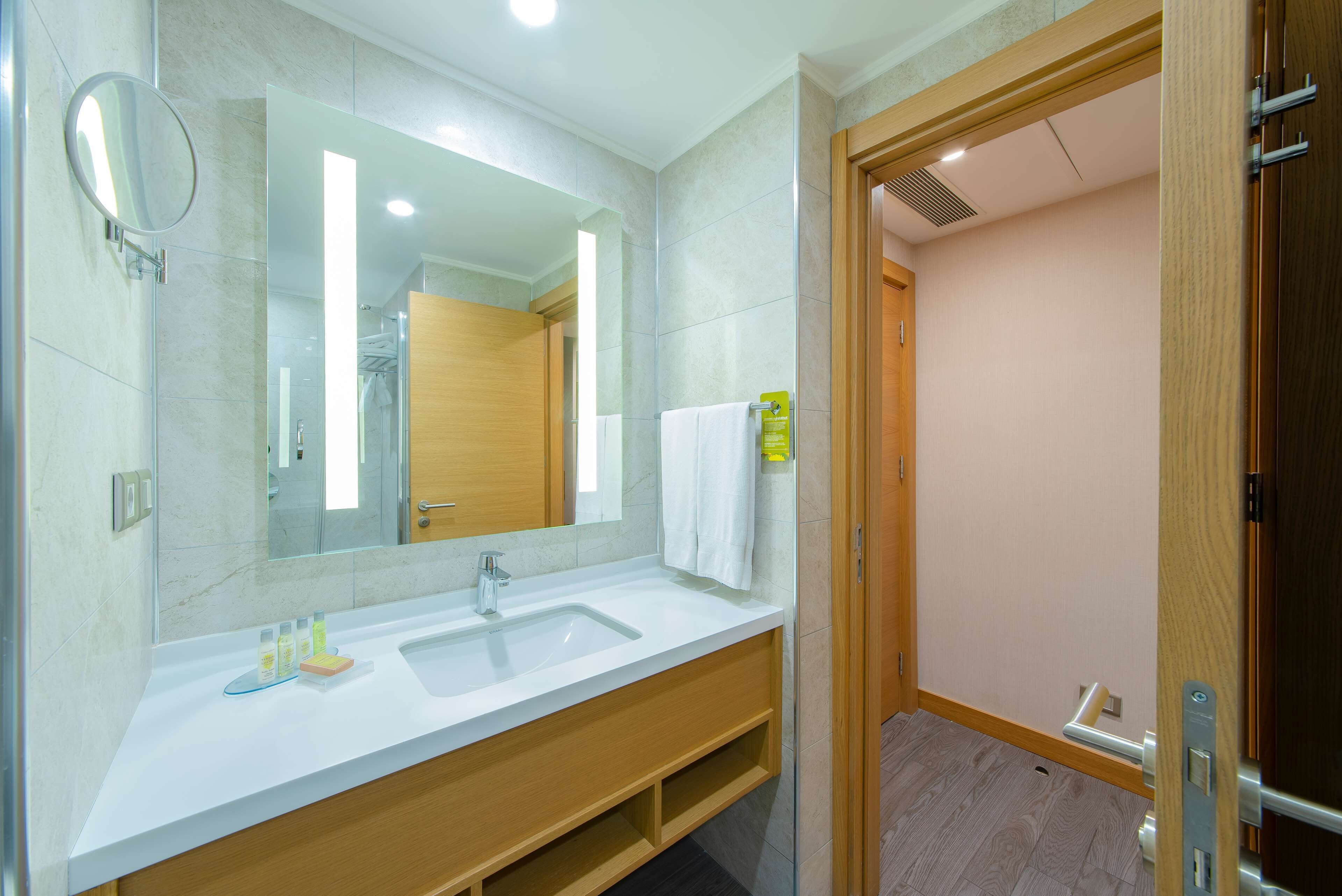 Een moderne badkamer met een grote spiegel, een wit wastafelmeubel en een houten opbergkast.