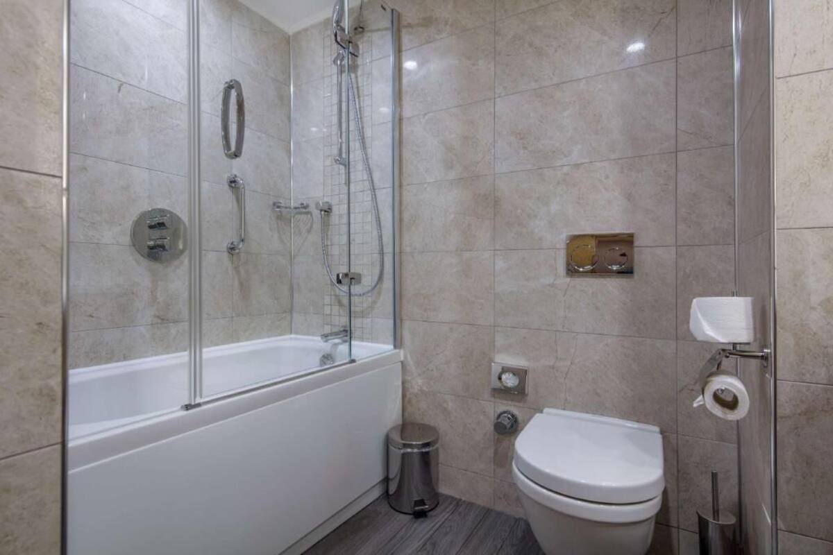 A modern bathroom with a glass-enclosed shower, a white bathtub, and a toilet.