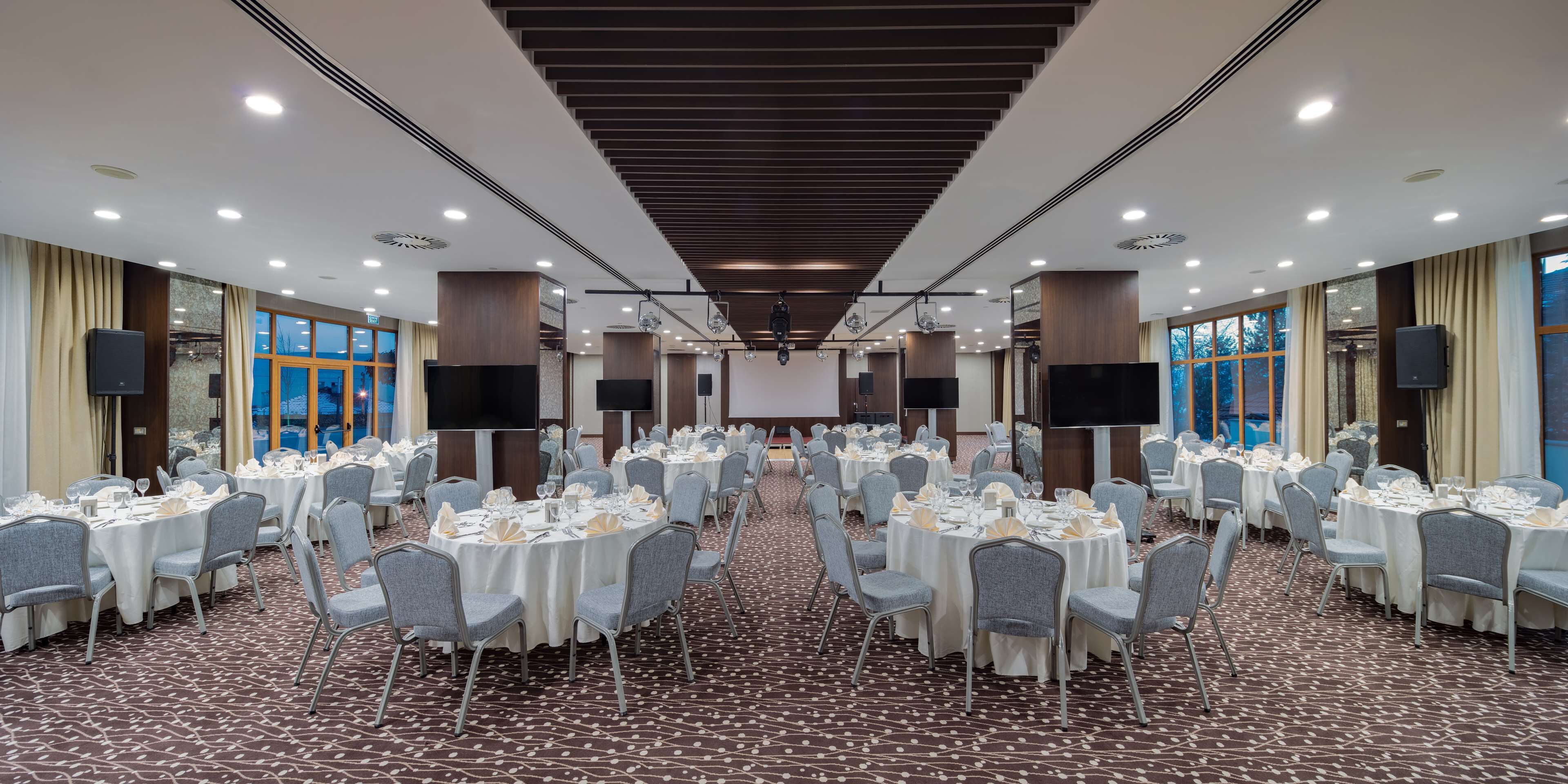 Un salón de banquetes con mesas redondas, sillas grises y una alfombra estampada.