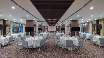 A banquet hall with round tables, grey chairs, and a patterned carpet.