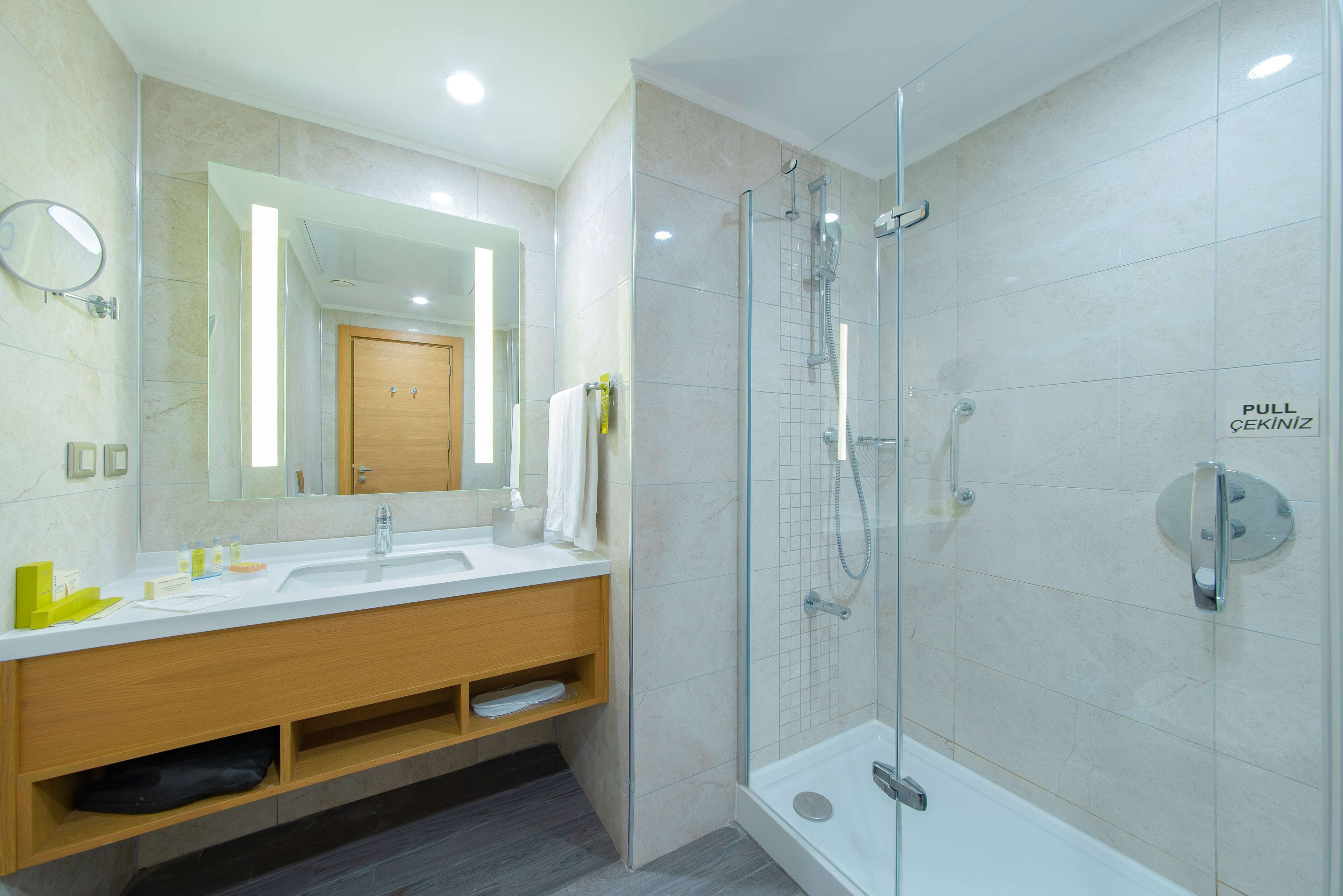 A modern bathroom with a glass-enclosed shower, a large mirror, and a white sink.