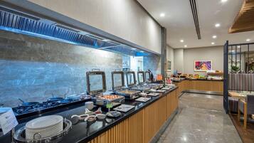 Uma área de buffet com parede de mármore, fogão e diversos alimentos.