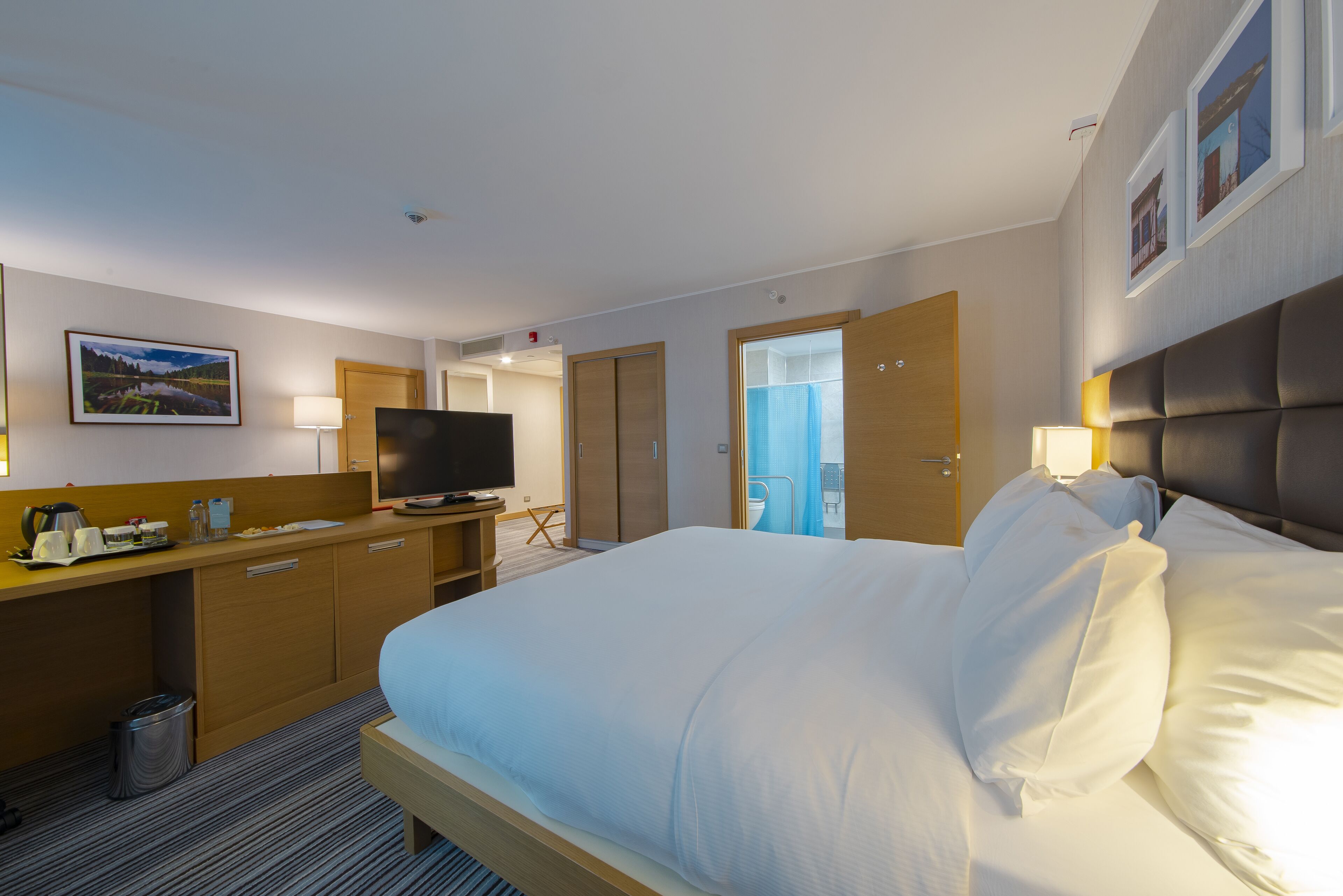 Habitación de hotel con cama, escritorio con televisor y baño visible a través de una puerta abierta.