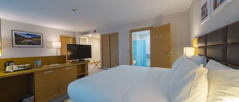 Habitación de hotel con cama, escritorio con televisor y baño visible a través de una puerta abierta.