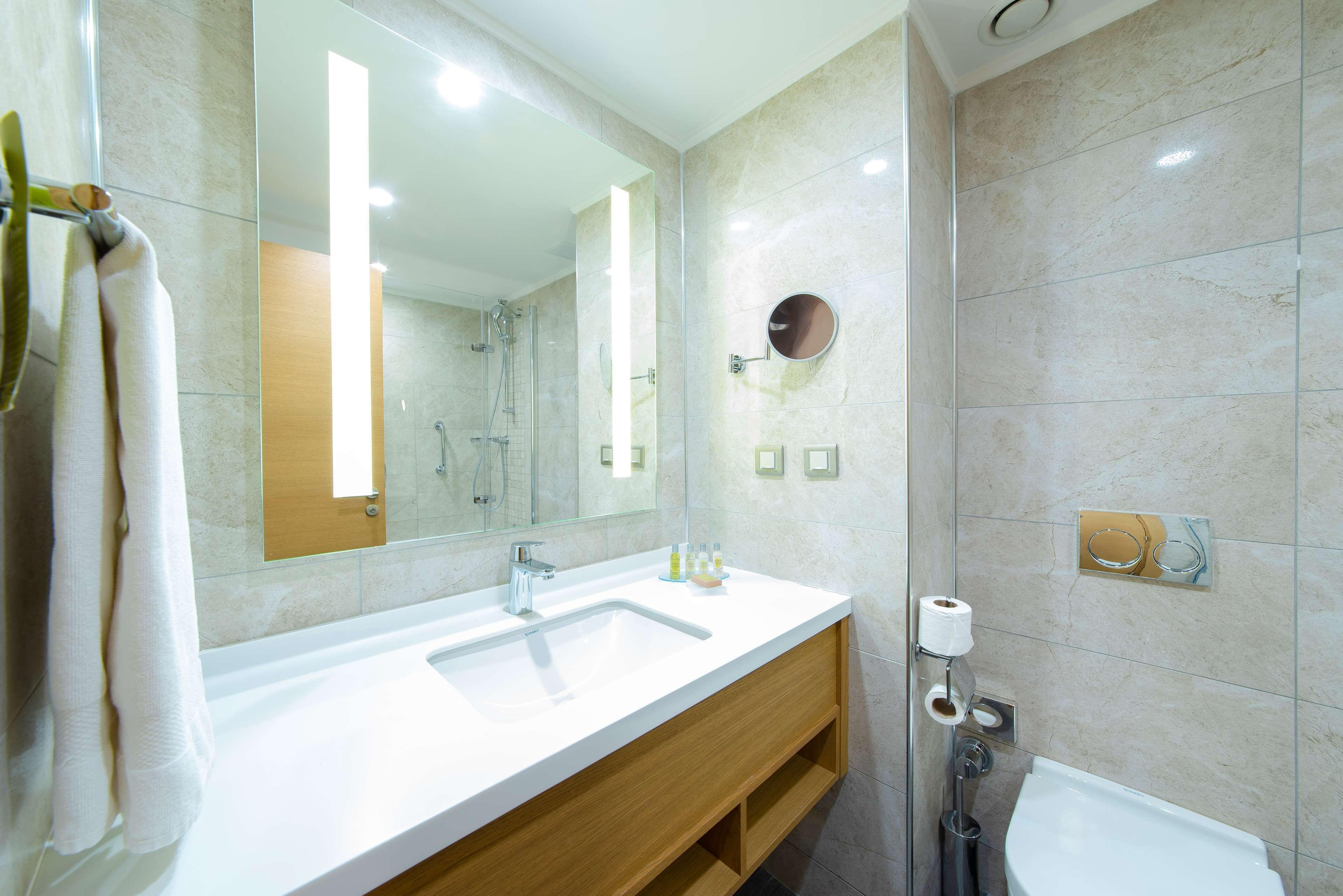 Un baño moderno con un espejo grande, un lavamanos, una ducha y un inodoro.