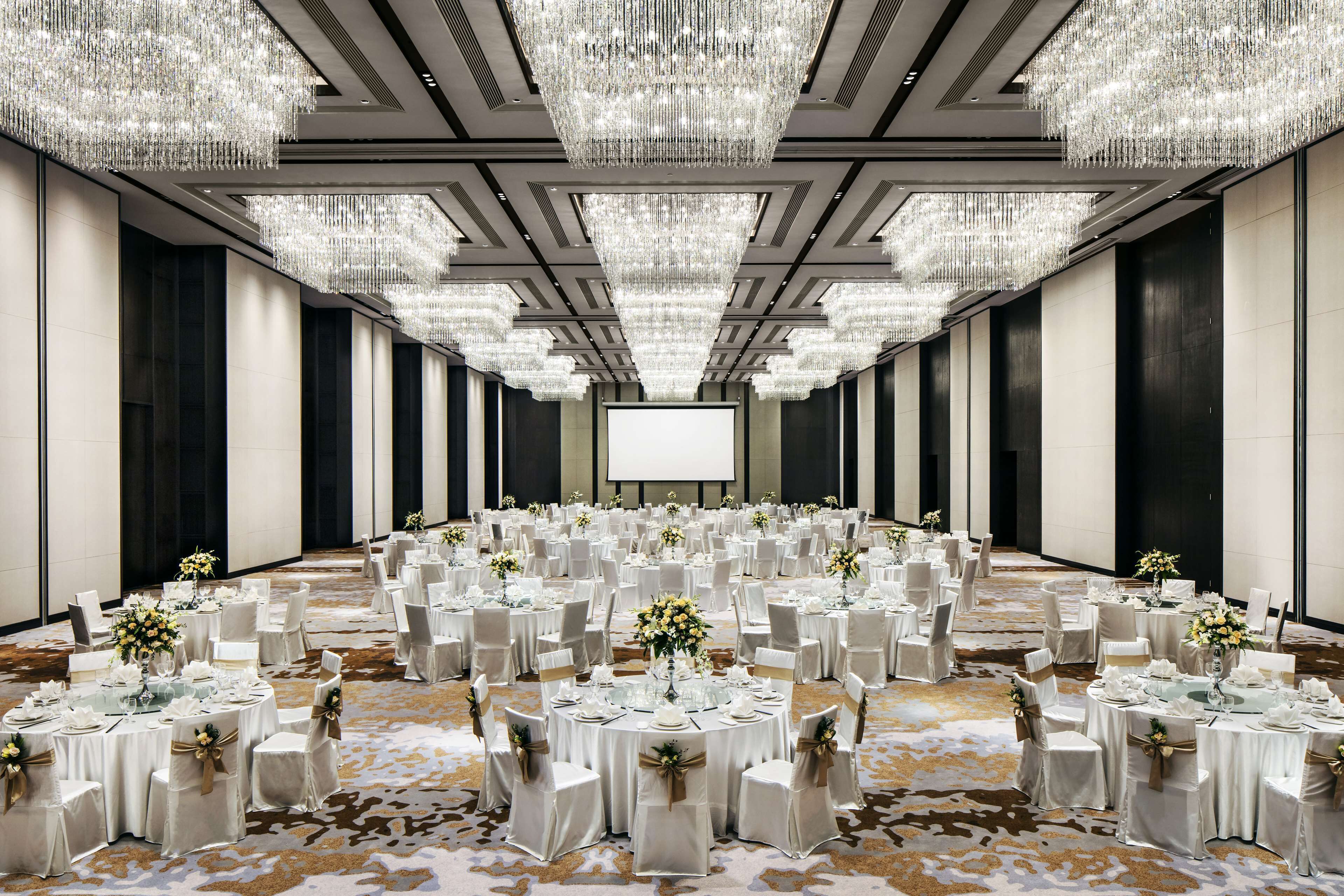 A banquet hall with round tables, white tablecloths, and chairs, decorated with floral centerpieces.