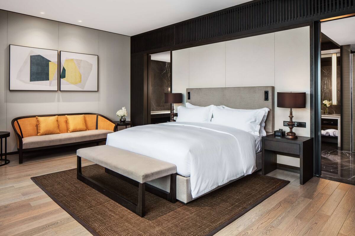 Un dormitorio moderno con una cama grande, un banco, un sofá y dos mesitas de noche con lámparas.