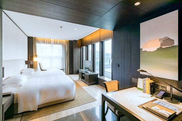 Une chambre d’hôtel moderne dotée d’un grand lit, d’un bureau avec un ordinateur, d’une télévision et d’une grande fenêtre donnant sur la ville.