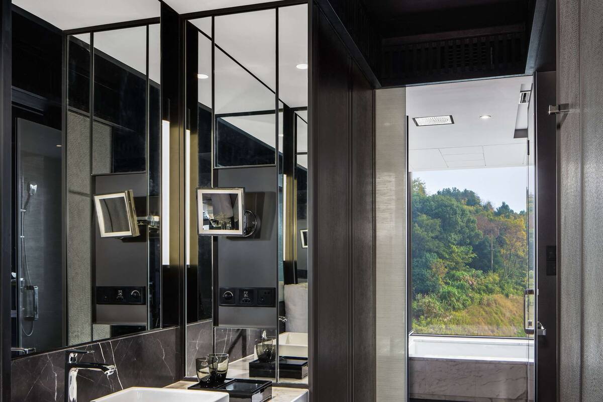 Un baño moderno con un espejo grande, dos lavamanos y vistas a una zona boscosa.