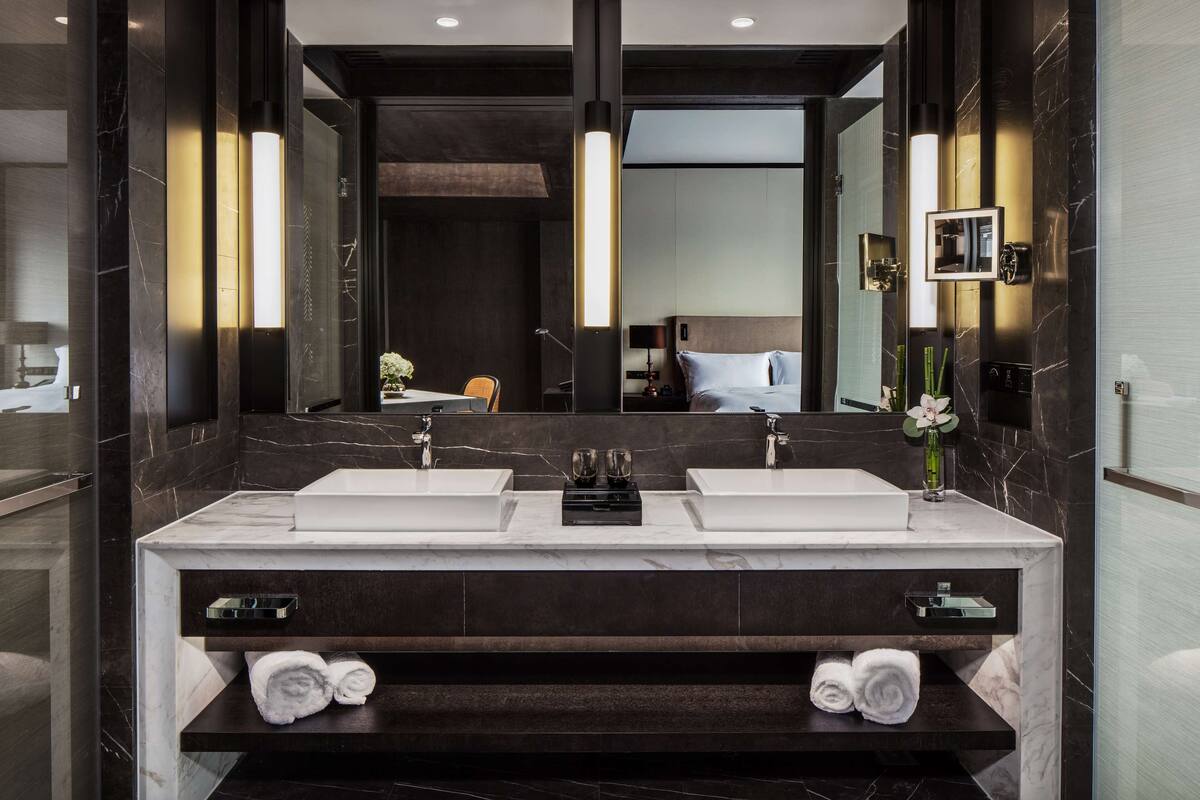 Un baño moderno con dos lavamanos, paredes de mármol oscuro y un espejo grande.