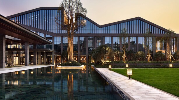 Een modern gebouw met een reflecterend zwembad, een overdekte doorgang en verzorgde groenvoorziening.