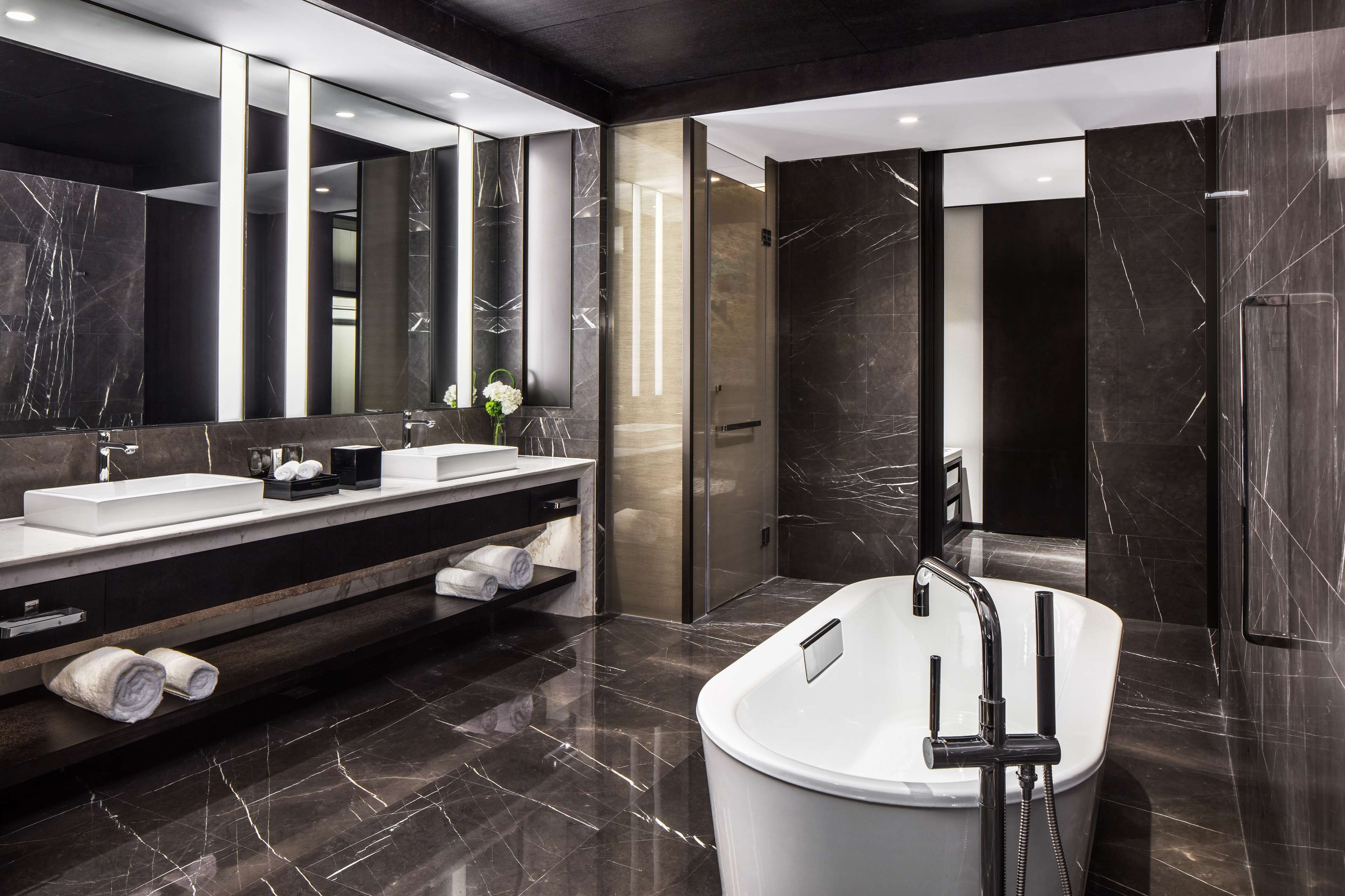 Un baño moderno con un espejo grande, dos lavamanos, una bañera y suelo de mármol.