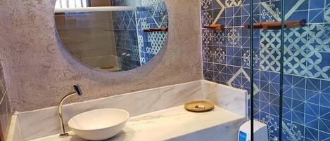 Une salle de bain avec un miroir rond, un lavabo blanc en forme de cuvette et un distributeur de savon liquide. Les murs sont recouverts de carreaux aux motifs bleus et blancs.