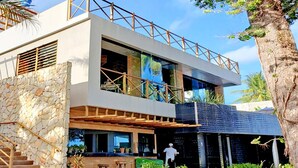 Un bâtiment moderne à deux étages, doté d’une façade en pierre, d’une terrasse en bois et d’un espace extérieur couvert avec des sièges.