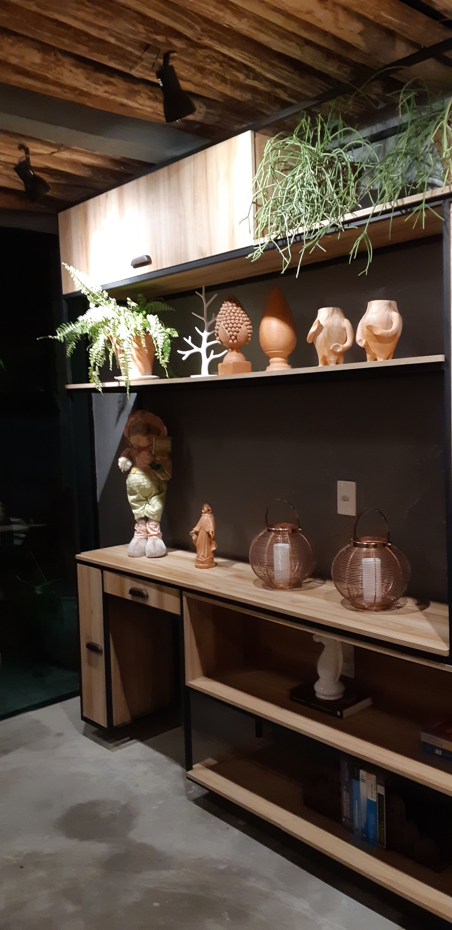 A wooden desk with shelves holding decorative items, including a plant, pottery, and a statue.