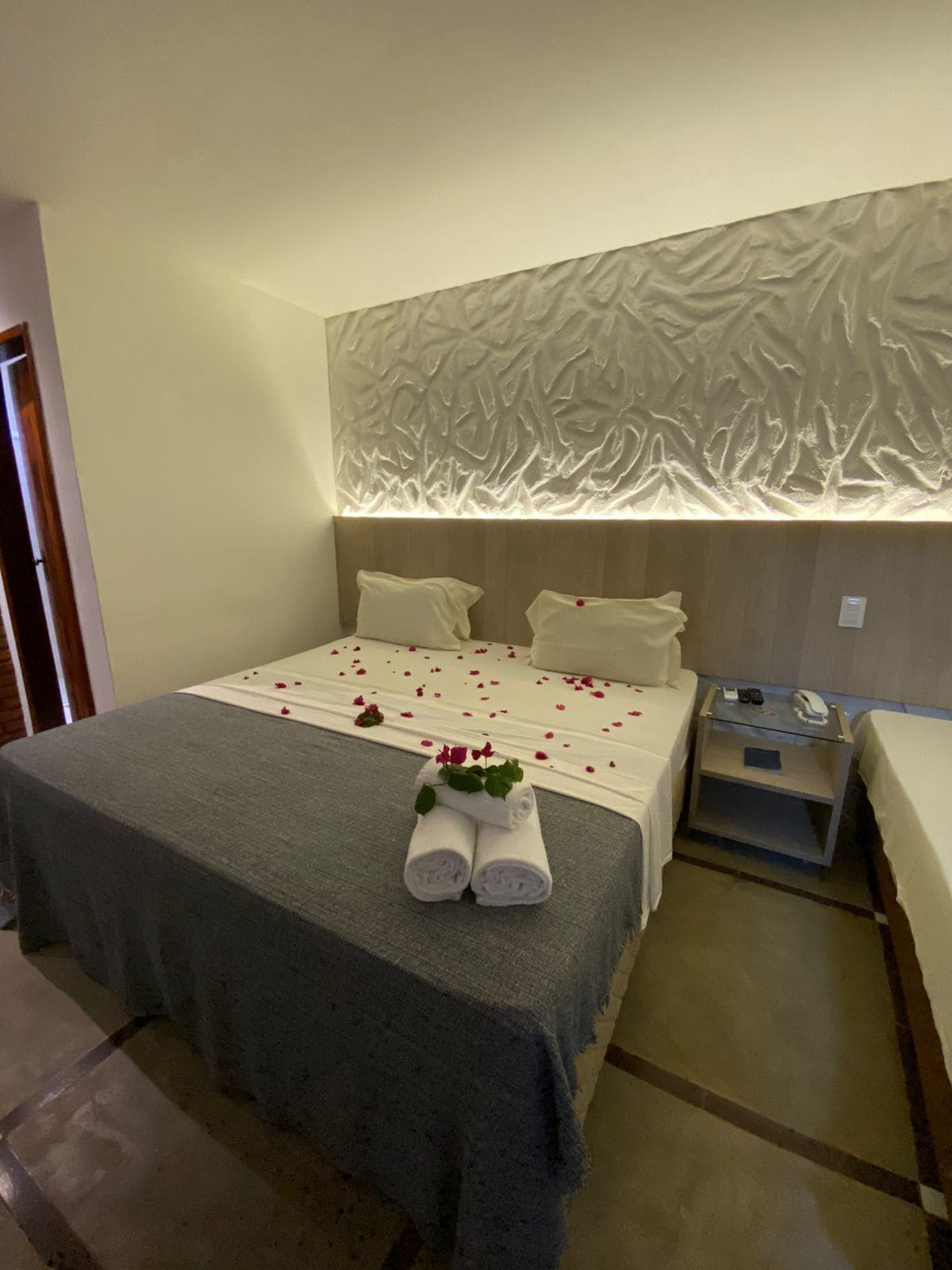 Quarto de hotel com uma cama, mesa de cabeceira e parede com design texturizado.