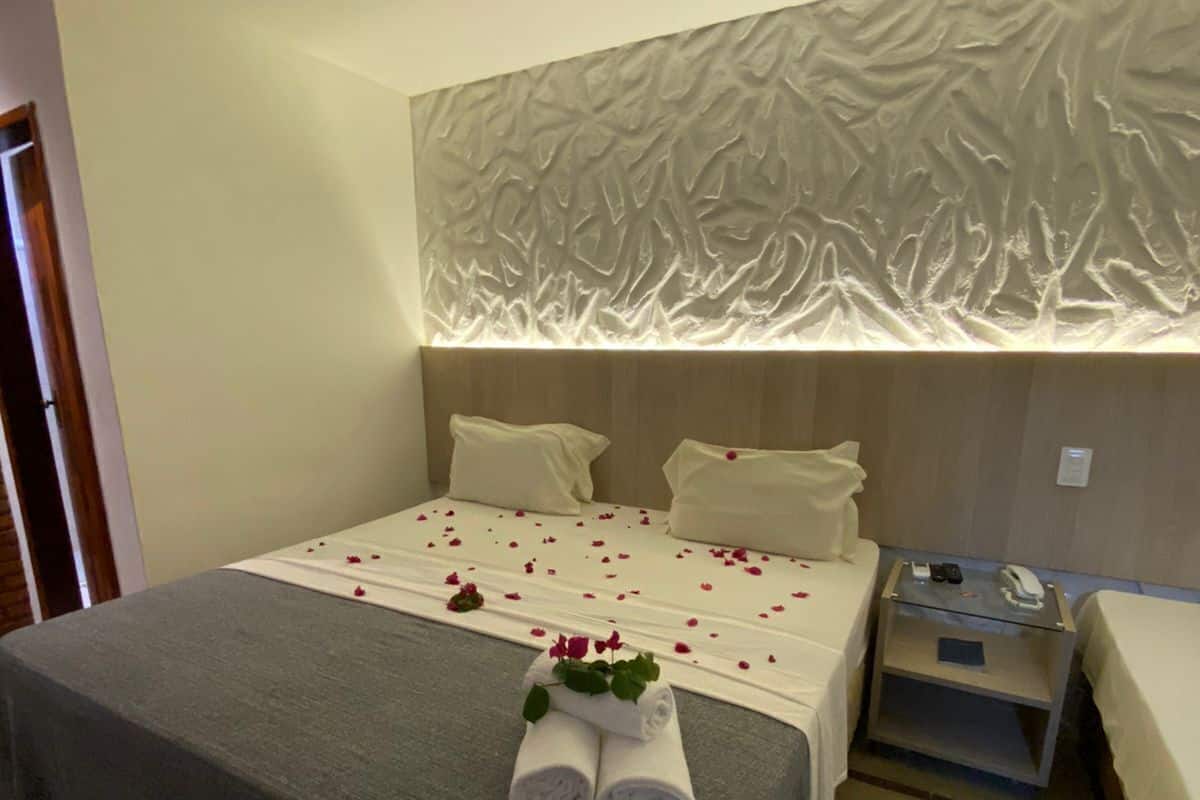 Una habitación de hotel con cama, mesita de noche y una lámpara fijada en la pared.