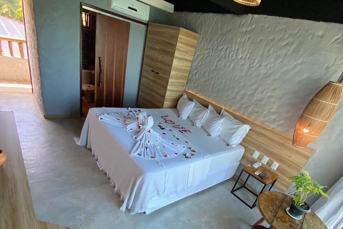 Un dormitorio con cama, mesita de noche, sillón y una pequeña mesa con una planta.