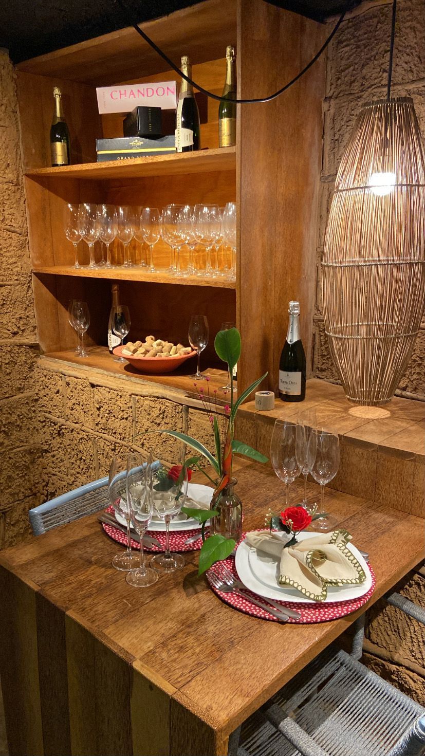 A wooden table set with plates, cutlery, and wine glasses, with a bottle of wine and a basket of bread on the table.