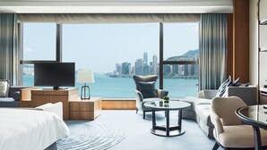 A hotel room with a large window offering a city view, a flat-screen TV, a sofa, a coffee table, and a bed. - Kerry Hotel Hong Kong by Shangri-la (Kowloon)