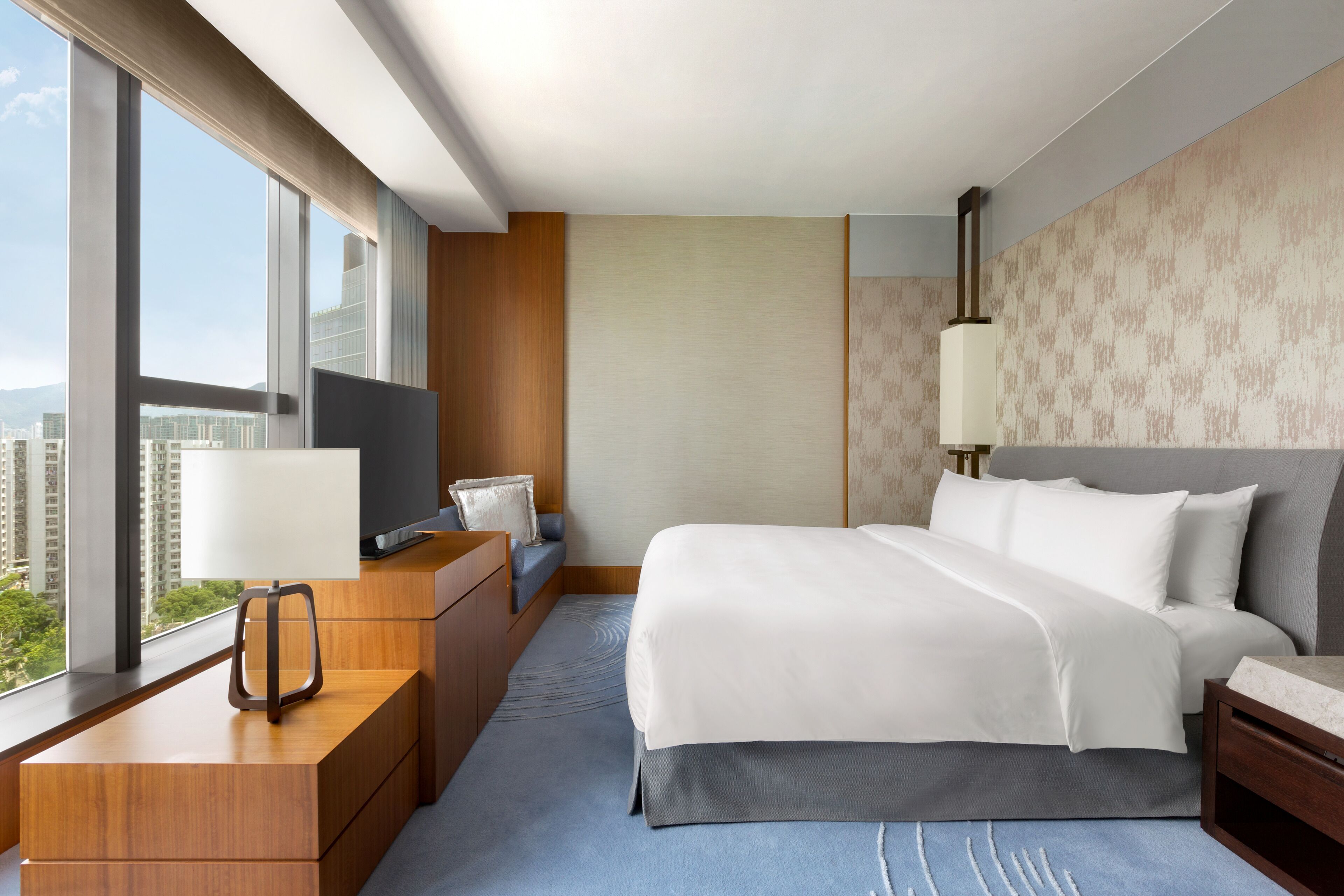 Une chambre d’hôtel moderne dotée d’un grand lit, d’un bureau avec une télévision et offrant une vue sur la ville grâce à de grandes fenêtres.