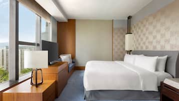A modern hotel room with a large bed, a desk with a TV, and a view of the city through large windows.