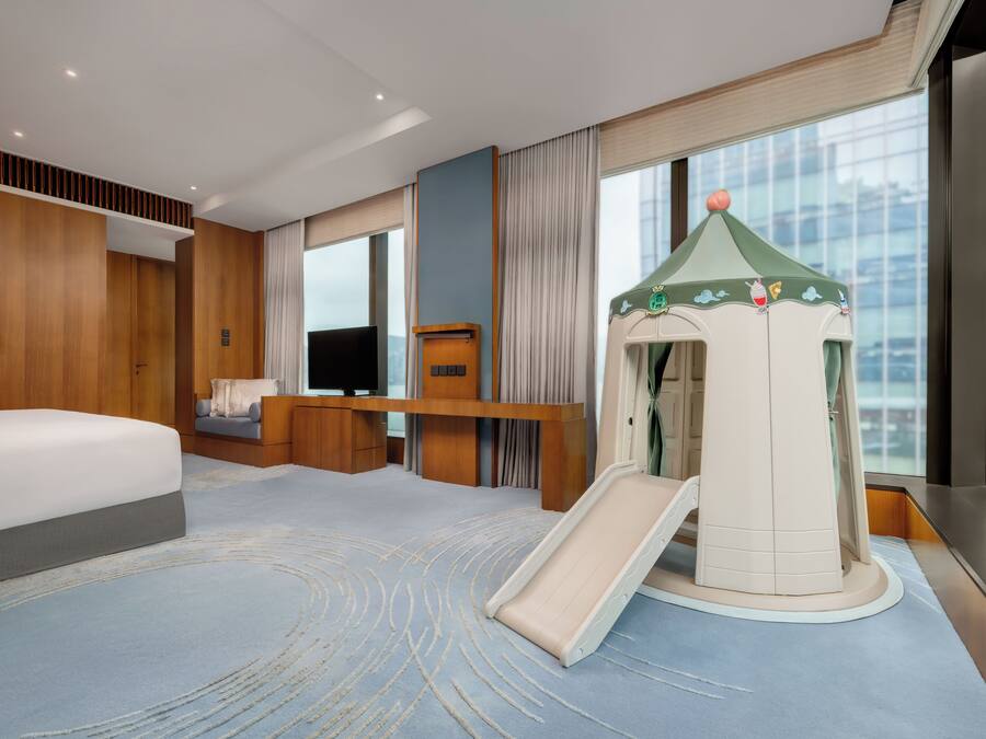 A hotel room with a bed, a desk, a TV, a slide, and a view of the city.