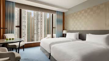 A hotel room with two beds, a dining table, and a view of high-rise buildings.
