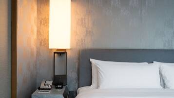 Une chambre d’hôtel avec un lit, une table de chevet avec un téléphone et une horloge, et une lampe fixée au mur.