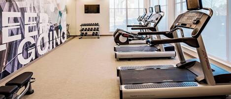 A gym with treadmills, dumbbells, and a wall with motivational text.