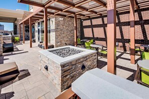Un espacio al aire libre con un patio de piedra, asientos de piedra, un brasero y sillas verdes.
