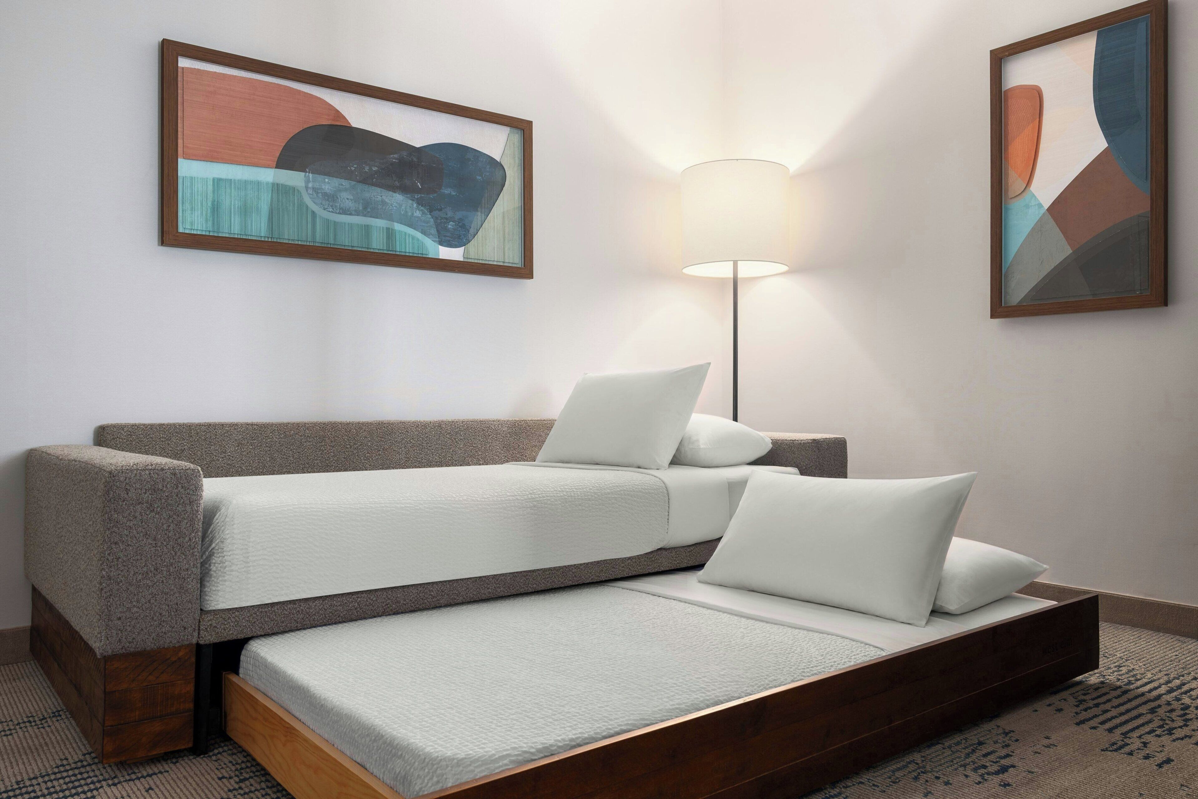 Una habitación con sofá cama, una lámpara de pie y dos cuadros abstractos en la pared.