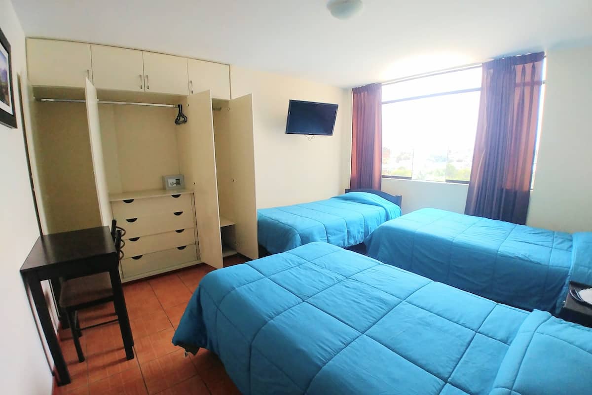 Ein Schlafzimmer mit zwei Betten, einem Schreibtisch, einem Kleiderschrank, einem Fernseher und einem Fenster mit Vorhängen.