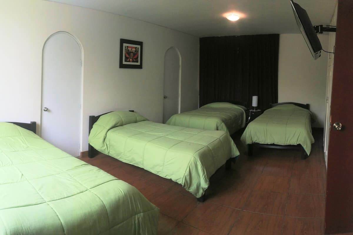 Ein Zimmer mit drei Einzelbetten, einem kleinen Schreibtisch und einem Stuhl.