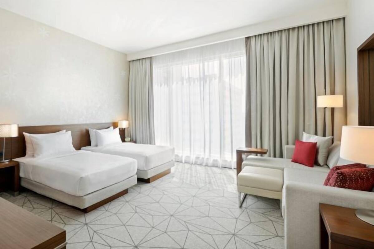 Een hotelkamer met twee bedden, een bank, een tafeltje en een lamp.