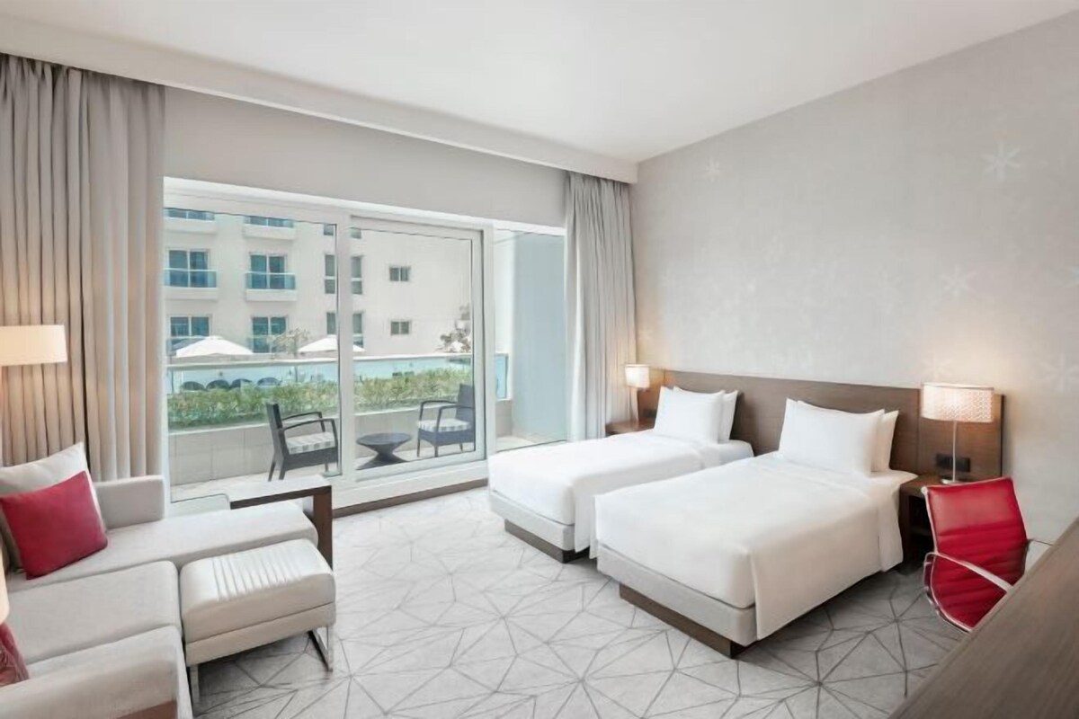 Habitación de hotel con balcón, dos camas, un sofá y un escritorio.