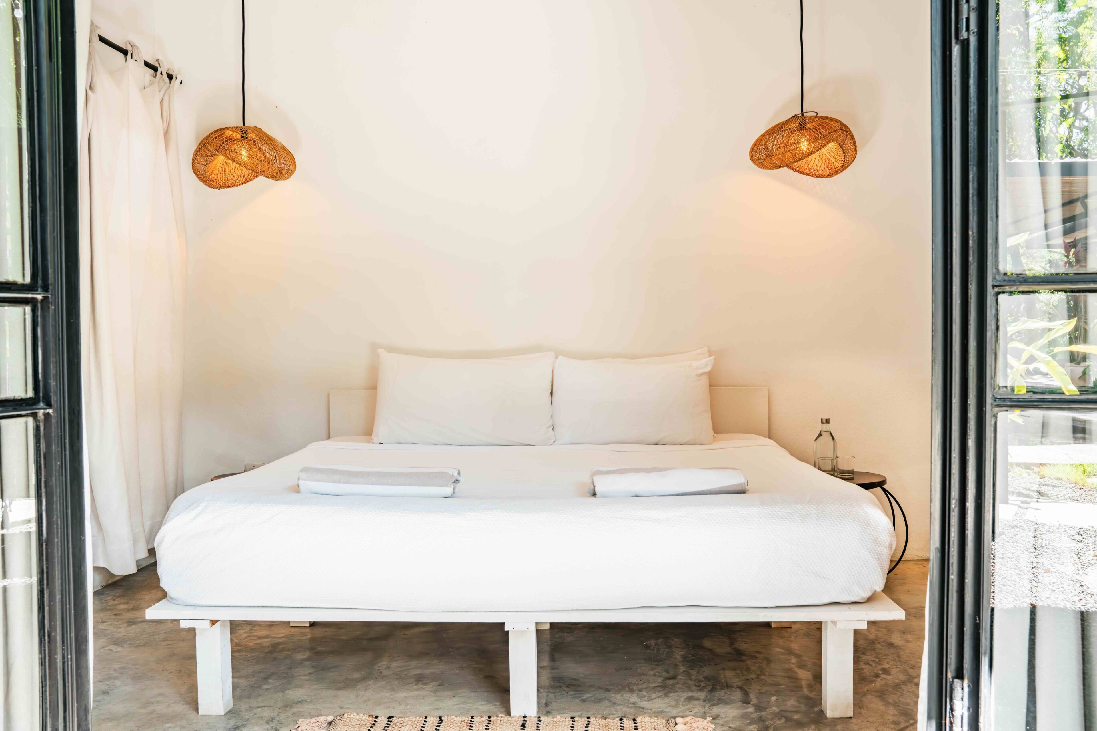 A bed with white bedding, two hanging lamps, and a window with a view.