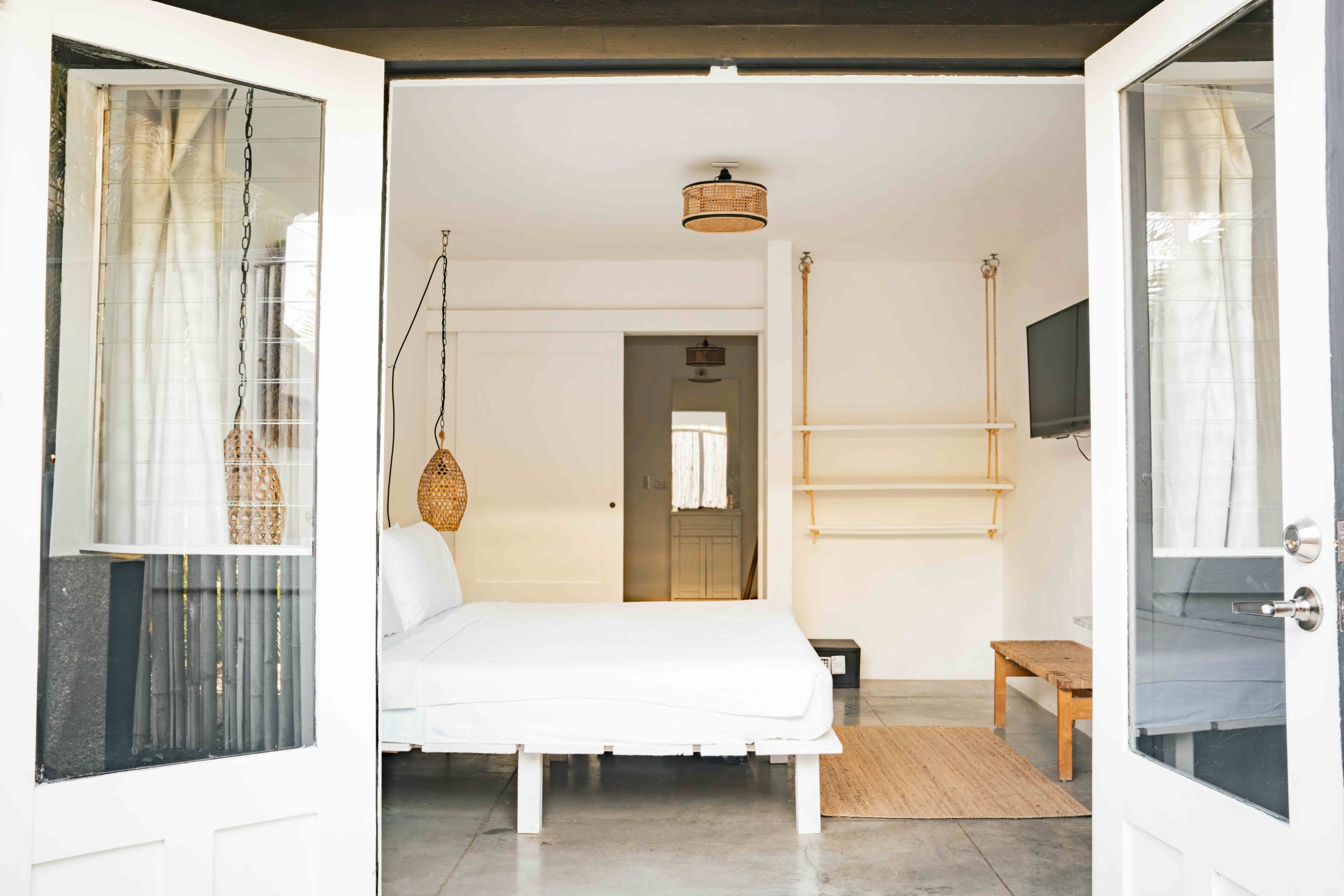 Un dormitorio con cama, una cesta colgante, un banco de madera y televisión.