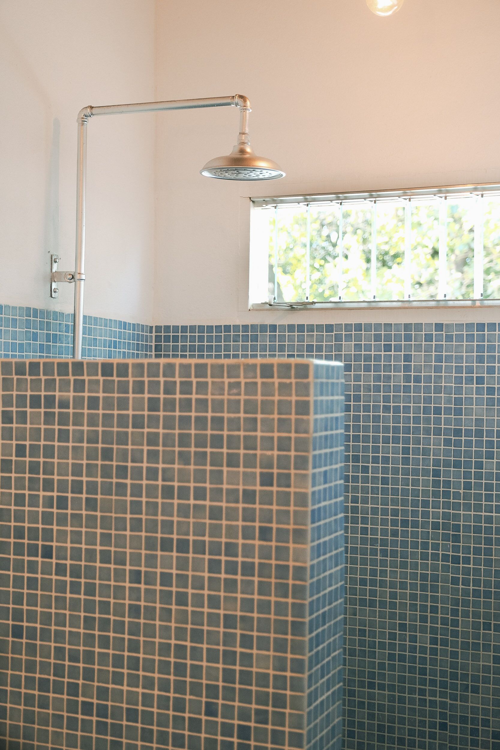A bathroom with a shower area, tiled walls, and a window with a view of greenery.