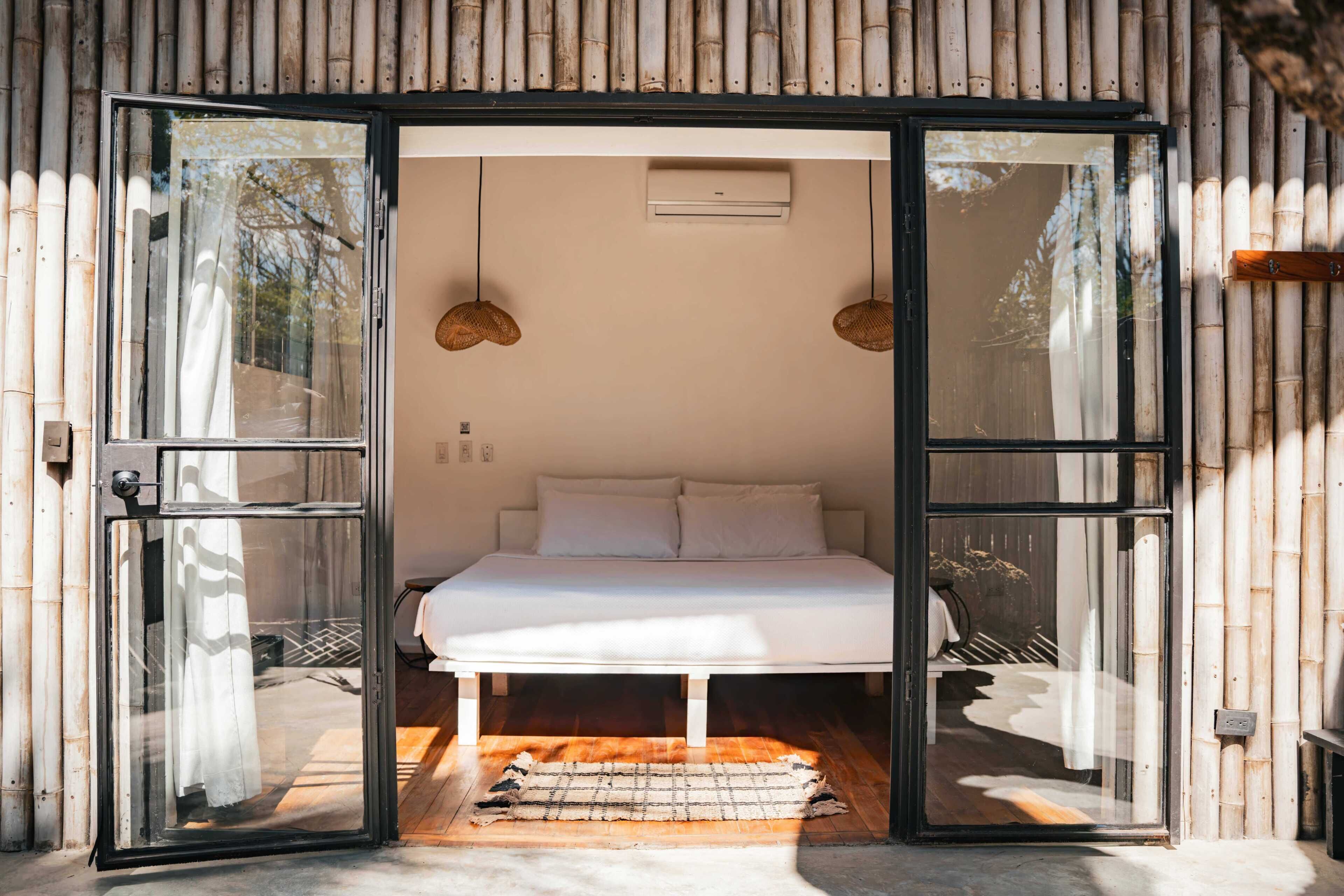 Una habitación con una cama, dos lámparas colgantes y un ventanal con pared de bambú.
