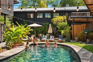 Una piscina rodeada de sillones de descanso y sombrillas, con un edificio al fondo.