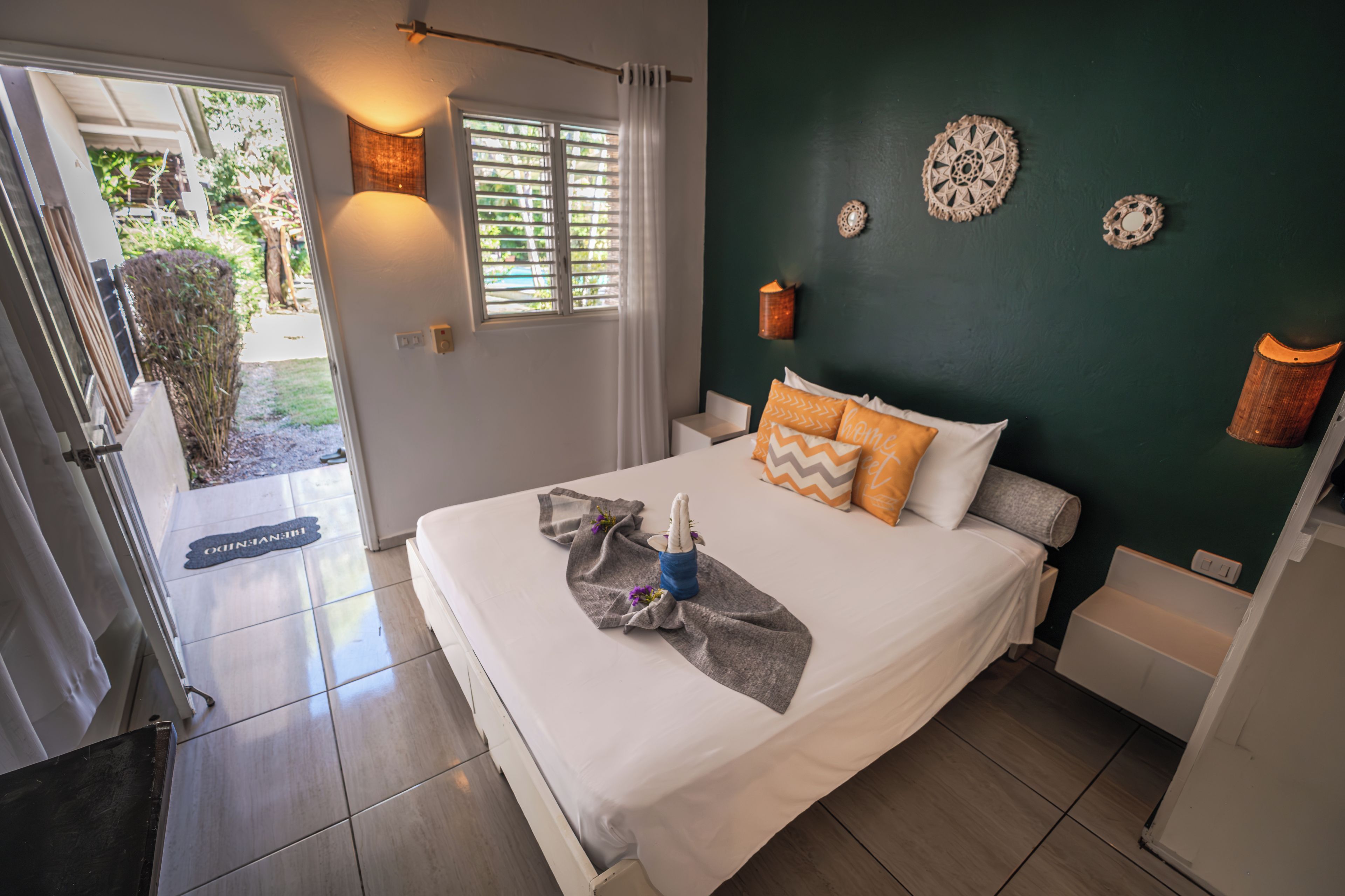 Een slaapkamer met een bed, nachtkastje, een wandlamp en een deur die leidt naar een balkon.