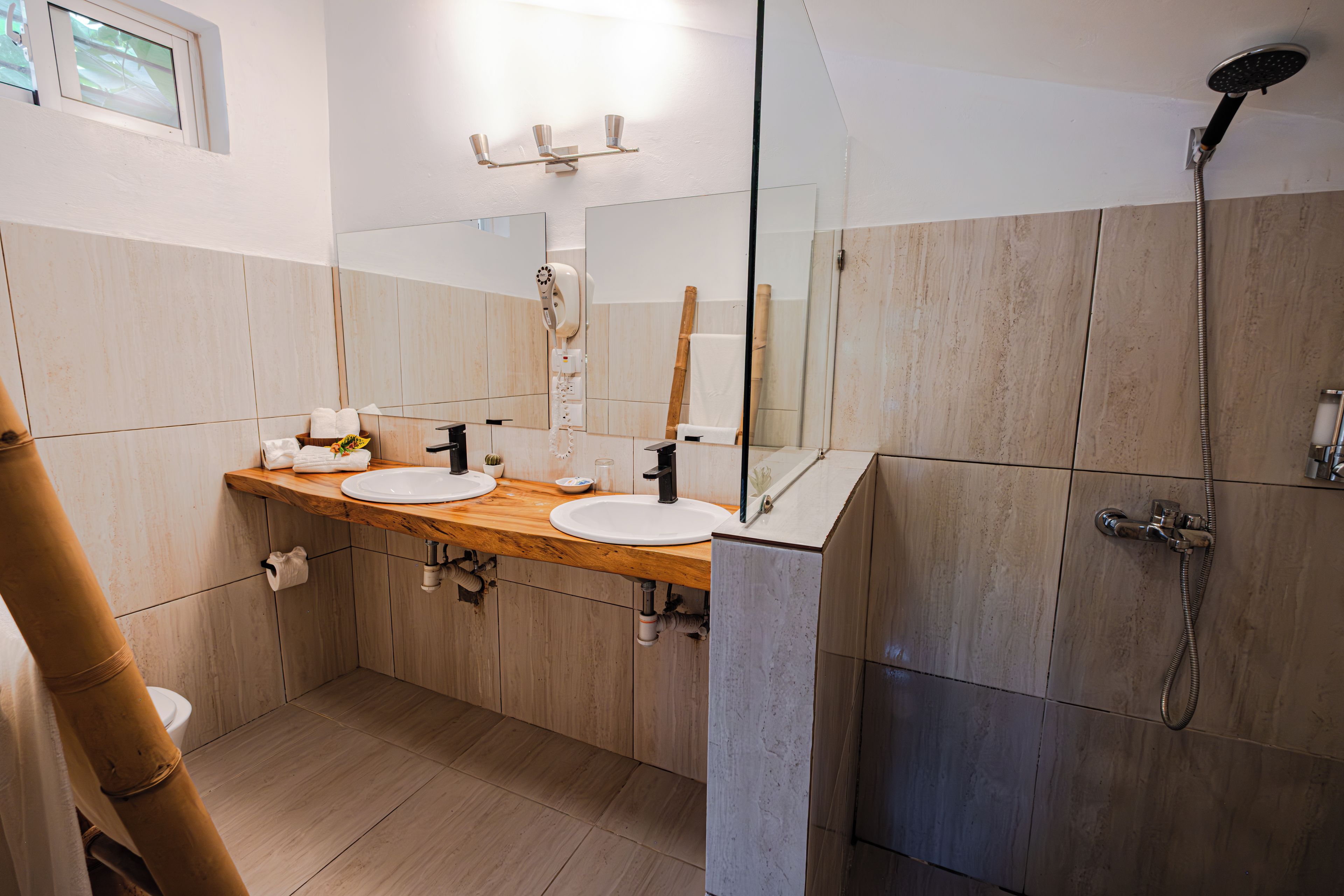 A modern bathroom with a wooden vanity, two sinks, a mirror, a shower, and a toilet.