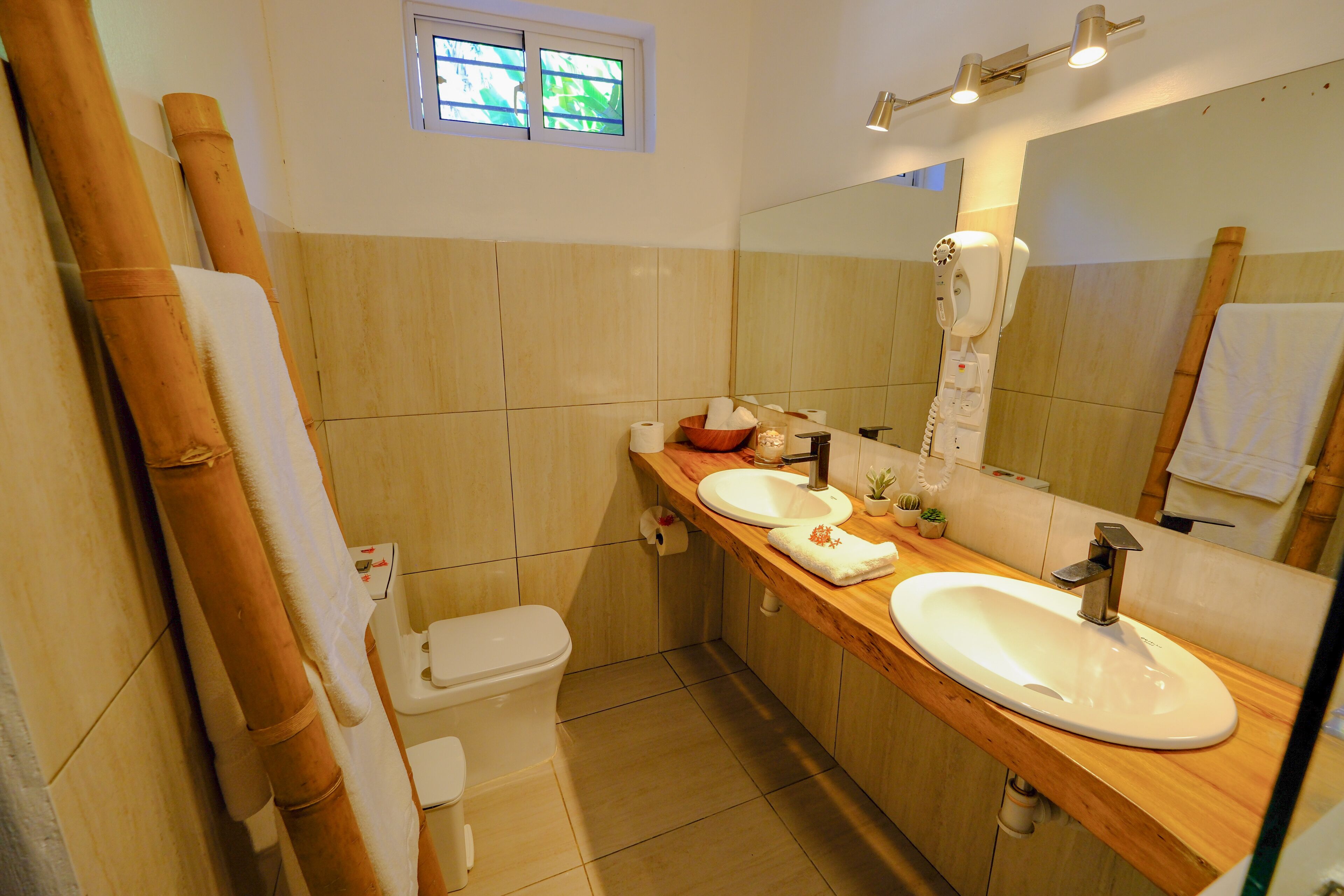 A bathroom with a wooden vanity, two sinks, a toilet, and a hairdryer.