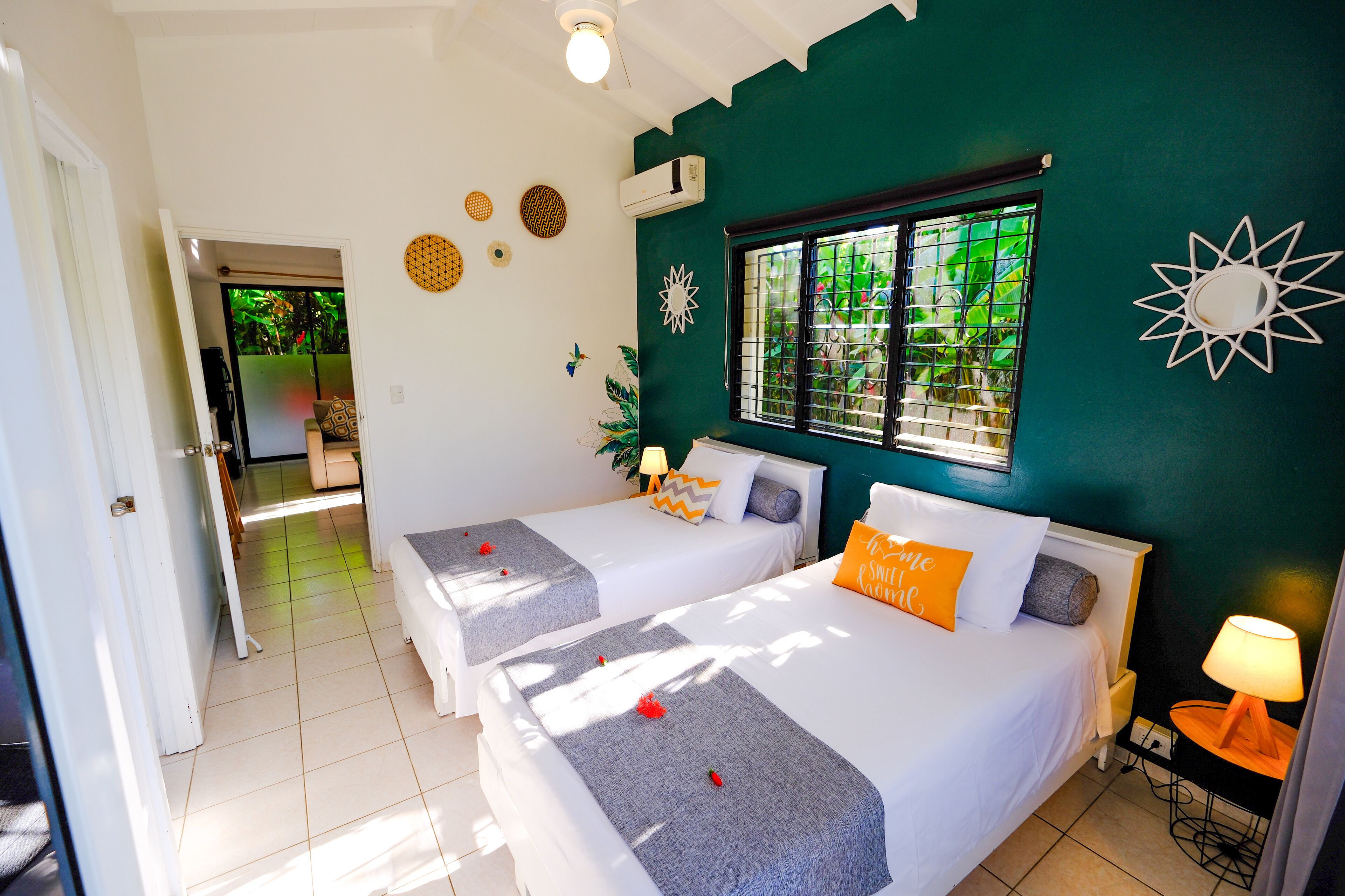 A room with two beds, a window with bars, a door leading to another room, and a wall-mounted air conditioner.