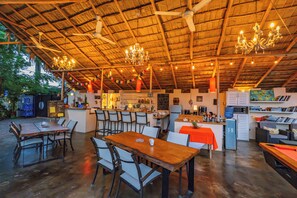 Un comedor interior con mesas y sillas de madera, una zona de bar con mostrador, y una cocina al fondo.