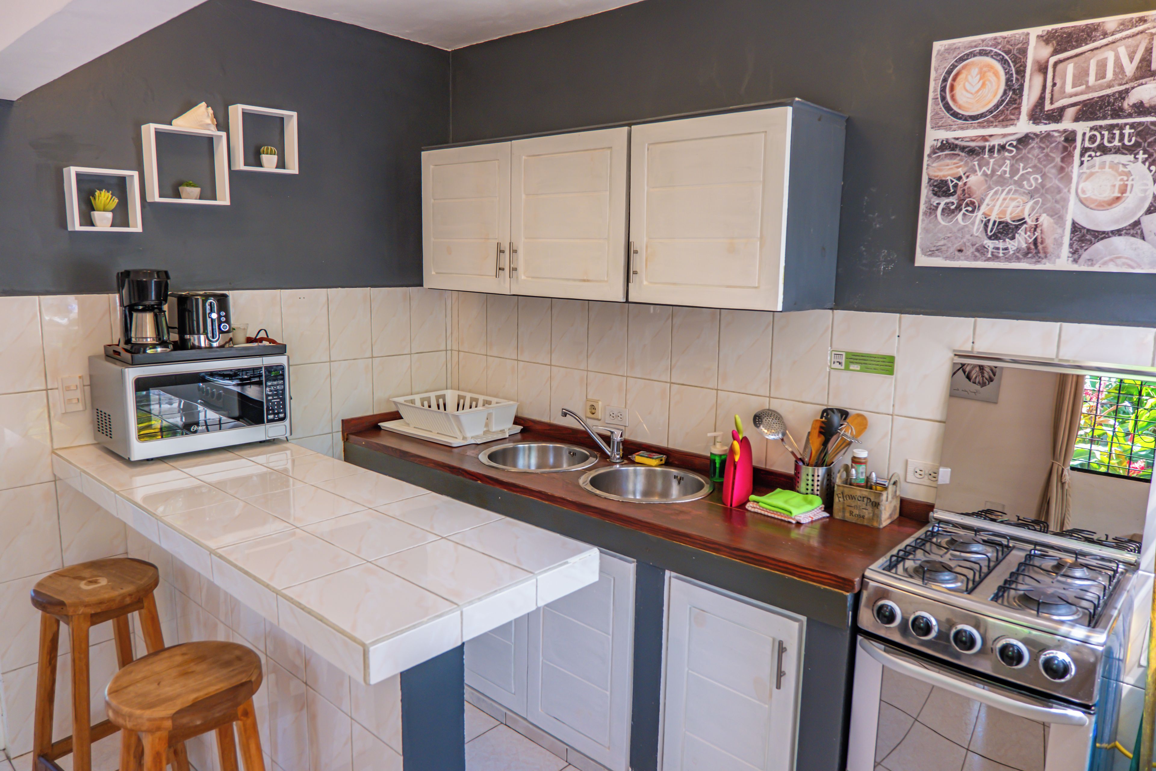 A compact kitchen with white cabinets, a gas stove, a coffee maker, and a sink.